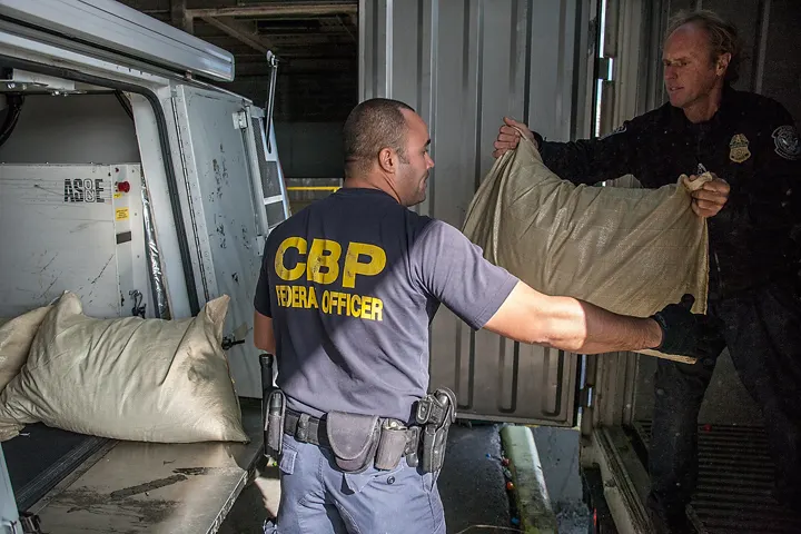 Two US customs officers unloading sacks from a shipping container for inspection